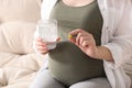 Pregnant woman holding pill and glass with water on sofa, closeup Royalty Free Stock Photo