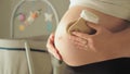 Pregnant woman holding tiny baby socks over her belly. Baby crib with spinning toys in the backgournd. Expecting and Royalty Free Stock Photo