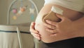 Pregnant woman holding tiny baby socks over her belly. Baby crib with spinning toys in the backgournd. Expecting and Royalty Free Stock Photo