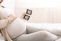 Pregnant woman holding ultrasound photo of baby and caressing her belly Royalty Free Stock Photo