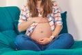 A pregnant woman in jeans and a tank top with a shirt on the background of a blue sofa. Stylish casual clothes of a