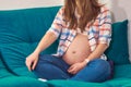 A pregnant woman in jeans and a tank top with a shirt on the background of a blue sofa. Stylish casual clothes of a