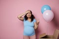 Pregnant woman holds her head, amazed expecting twins, boy and girl, isolated on pink . Baby shower. Gender reveal party Royalty Free Stock Photo