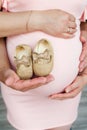 A pregnant woman holds small golden slippers near her tummy for her unborn baby. Hands of parents. Pregnancy.