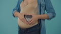 A pregnant woman holds an ultrasound scan, near her stomach, with her hands folded in the shape of a heart. Bloated