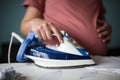 Pregnant woman at home ironing baby laundry. Royalty Free Stock Photo