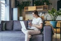 Pregnant woman at home sitting on sofa uses laptop for video call, working remotely Royalty Free Stock Photo