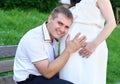 Pregnant woman and husband, man listen belly and talk with baby, happy family, couple in city park, summer season, green grass and