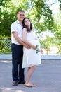 Pregnant woman with husband posing in the city park, family portrait, summer season, green grass and trees Royalty Free Stock Photo