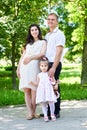 Pregnant woman with husband posing in the city park, family portrait, summer season, green grass and trees Royalty Free Stock Photo