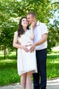 Pregnant woman with husband posing in the city park, family portrait, summer season, green grass and trees Royalty Free Stock Photo