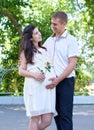 Pregnant woman with husband posing in the city park, family portrait, summer season, green grass and trees Royalty Free Stock Photo