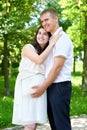 Pregnant woman with husband posing in the city park, family portrait, summer season, green grass and trees Royalty Free Stock Photo