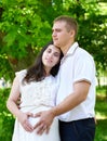 Pregnant woman with husband posing in the city park, family portrait, summer season, green grass and trees Royalty Free Stock Photo