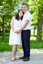 Pregnant woman with husband posing in the city park, family portrait, summer season, green grass and trees Royalty Free Stock Photo