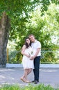 Pregnant woman with husband posing in the city park, family portrait, summer season, green grass and trees Royalty Free Stock Photo