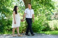 Pregnant woman with husband walking in the city park, family portrait, summer season, green grass and trees Royalty Free Stock Photo