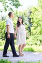 Pregnant woman with husband walking in the city park, family portrait, summer season, green grass and trees Royalty Free Stock Photo