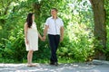 Pregnant woman with husband walking in the city park, family portrait, summer season, green grass and trees Royalty Free Stock Photo