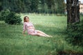 Pregnant woman inpink dress sitting on grass and touching bump whilst holding pink rose girl waiting