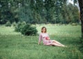 Pregnant woman inpink dress sitting on grass and touching bump whilst holding pink rose girl waiting