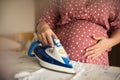 Pregnant woman ironing baby laundry at home. Preparing for baby Royalty Free Stock Photo