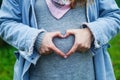 Pregnant woman in jeans jacket holding her hands in a heart shape Royalty Free Stock Photo