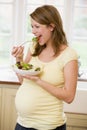 Pregnant woman in kitchen eating a salad smiling Royalty Free Stock Photo