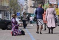 Pregnant woman kneeling on a pavement and begging, passers-by walking by her