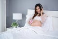 Pregnant woman listening to fetal heart sound through headphones on bed