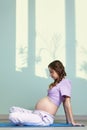 A pregnant woman with long brown hair sits cross-legged, meditating and practicing yoga during pregnancy. Woman looks at her