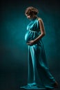 Pregnant woman in long silk dress over blue art background.