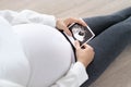 A pregnant woman is looking at an ultrasound photo of fetus. Mother gently touches the baby on stomach. Royalty Free Stock Photo