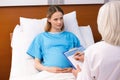 Pregnant woman lying in hospital bed and looking at doctor writing in clipboard Royalty Free Stock Photo