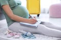 Pregnant woman making list while packing suitcase for maternity hospital at home