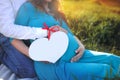 A pregnant woman and a man hold a paper heart with room for text. Copy space.