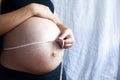 A pregnant woman measuring her belly with a tape