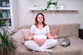 Pregnant woman meditates in the lotus position in the home interior, lifestyle