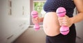 Pregnant woman mid section with pink weights in blurry hallway Royalty Free Stock Photo