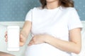 Pregnant woman with mobile phone in her hands in her bedroom . Motherhood , technology and love, using technology and staying at Royalty Free Stock Photo