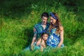 Pregnant woman mother to be in wreath and blue dress sitting with her daughter and husband in high green grass in sunset time in Royalty Free Stock Photo