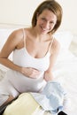 Pregnant woman packing baby clothing in suitcase