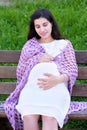 Pregnant woman portrait on outdoor, happy maternity concept, sit on bench in city park, summer season, green grass background Royalty Free Stock Photo