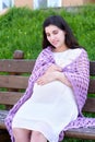 Pregnant woman portrait on outdoor, happy maternity concept, sit on bench in city park, summer season, green grass background Royalty Free Stock Photo