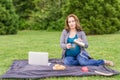 Pregnant woman pouring coffee otr tea from stainless thermos in the park after working on a computer. Royalty Free Stock Photo