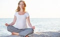 Pregnant woman practicing yoga in lotus position on beach at sun Royalty Free Stock Photo