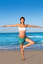 Pregnant woman precticing yoga in blue beach