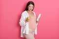 Pregnant woman with pretty stomach holding green apple and bottle of milk, expectant mother looking down, posing isolated over Royalty Free Stock Photo