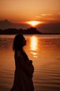 Pregnant woman in profile at sunset. Side view of silhouette in rays of setting sun reflected in water of beautiful