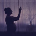 Pregnant woman raised her hands up asking for help. Pregnancy problems, silhouette of the expectant mother at the night window in Royalty Free Stock Photo